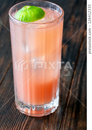 Guava Collins cocktail sparkles in tall glass with lime against dark backdrop 126412335