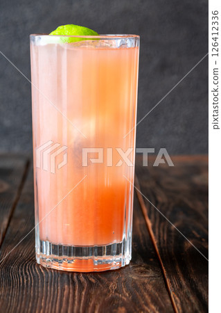 Guava Collins cocktail sparkles in tall glass with lime against dark backdrop Guava Collins cocktail sparkles in tall glass with lime against dark backdrop 126412336