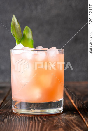 Guava rum punch cocktail with pineapple garnish on moody tropical evening backdrop Guava rum punch cocktail with pineapple garnish on moody tropical evening backdrop 126412337