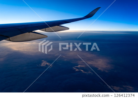 Experience the breathtaking view of a plane wing slicing through the serene clouds below during flight. Experience the breathtaking view of a plane wing slicing through the serene clouds below during flight. 126412374