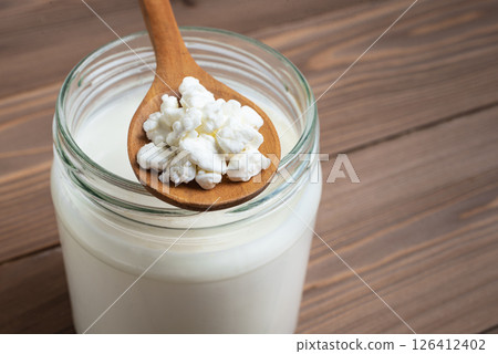 Milk kefir grains on wooden spoon and jar of kefir 126412402