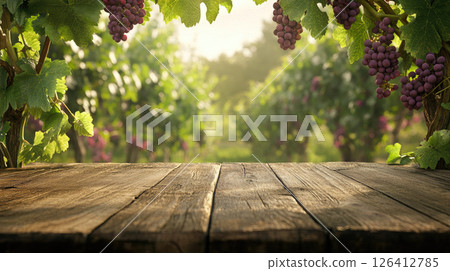 Purple grapes dangle above empty wooden tabletop with sun-drenched vineyard in background. Ideal for wine-related promotions or product placements 126412785