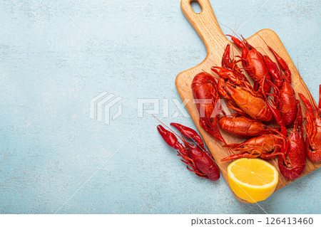 Cooked crayfish lying on wooden cutting board with lemon top view on blue background, copy space 126413460