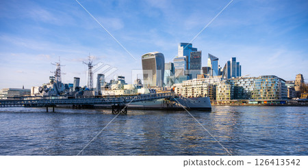 HMS Belfast is moored along the River Thames as modern buildings rise in the background. It showcases a blend of historic naval heritage and contemporary architecture in London. 126413542