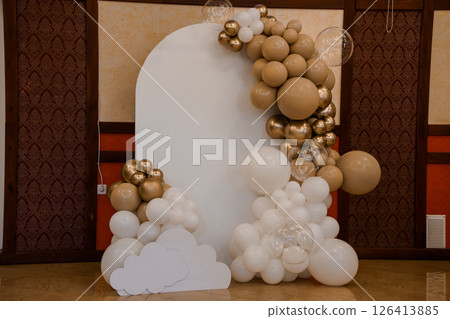 Elegant balloon arch backdrop with white base and beige, gold balloons for a luxurious event, decorated with transparent bubbles, creating a festive atmosphere 126413885