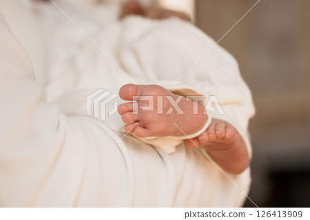 A tender moment showcasing a newborn baby s tiny foot gently held in a parent's arms, wrapped in soft, white fabric, symbolizing new life and parental love in a warm setting A tender moment showcasing a newborn baby s tiny foot gently held in a parent's arms, wrapped in soft, white fabric, symbolizing new life and parental love in a warm setting 126413909
