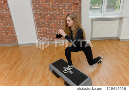 Young woman doing step-up workout on aerobic platform. 126414036