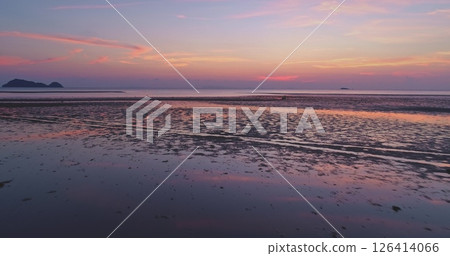 Aerial view of beautiful sunset reflecting on the wet sand of a tropical beach at low tide, creating a colorful and serene atmosphere with islands visible on the horizon 126414066