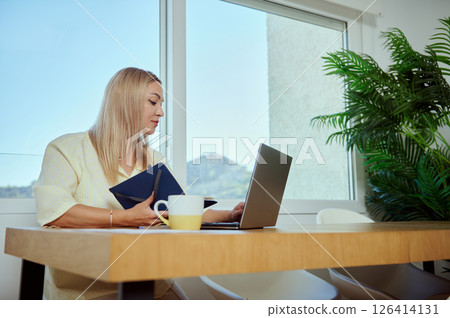 Woman Working Remotely on Laptop in Minimalist Home Office Interior Woman Working Remotely on Laptop in Minimalist Home Office Interior 126414131