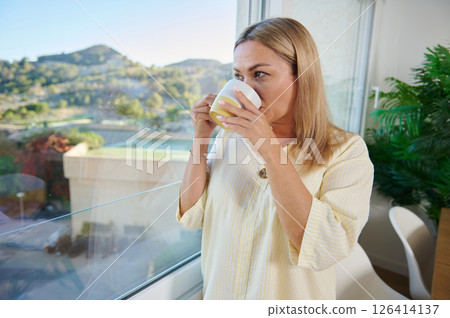 Woman Enjoying a Morning Drink by a Bright Window with Scenic View 126414137