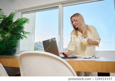 Home Office Setup Featuring Woman Working Remotely with Laptop and Coffee Home Office Setup Featuring Woman Working Remotely with Laptop and Coffee 126414147