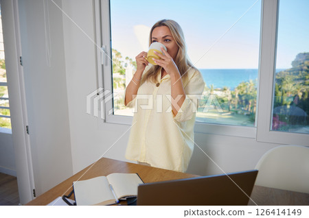 Woman Enjoying Coffee in a Sunny Home Office with Ocean View Woman Enjoying Coffee in a Sunny Home Office with Ocean View 126414149