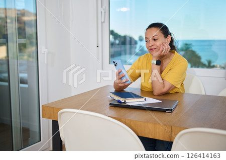 Woman Balancing Remote Work and Relaxation in a Minimalist Home With a Scenic Beach View 126414163