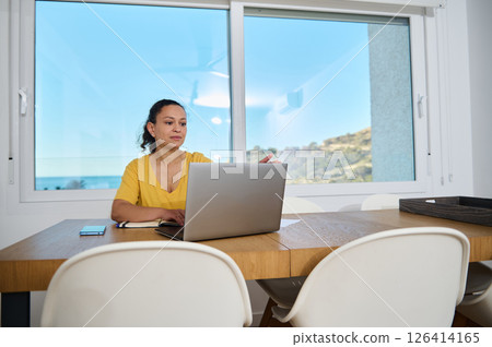 Woman Working Remotely on Laptop in Minimalist Home Office Interior With Scenic View Woman Working Remotely on Laptop in Minimalist Home Office Interior With Scenic View 126414165