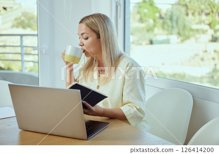 Woman Working Remotely with Laptop and Notebook in a Bright Home Office 126414200