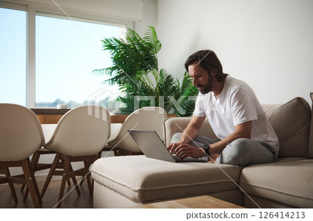 Man Working With Laptop in Minimalist Home Office Setting Man Working With Laptop in Minimalist Home Office Setting 126414213