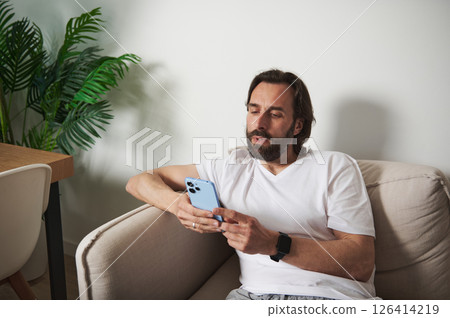 Man Relaxing in Minimalist Modern Home Using Smartphone for Communication 126414219