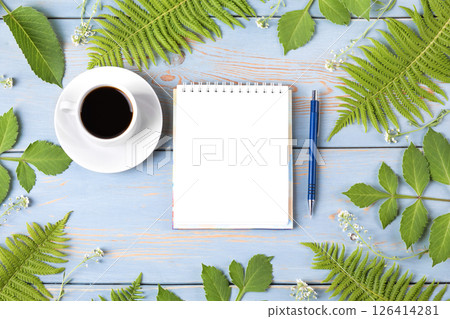 Summer composition with opened blank notepad, cup of black coffee, green leaves on wooden table. Morning coffee cup. 126414281