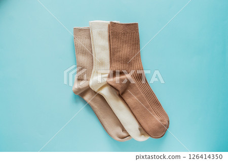 Three pairs of cozy socks in beige colors arranged neatly on soft blue background, showcasing texture and design for fashion and comfort enthusiasts 126414350
