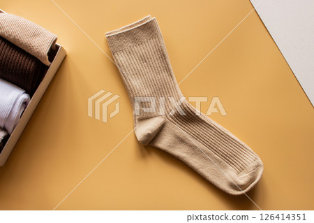 Beige sock pair positioned on vibrant yellow surface, with collection of folded socks nearby, highlighting fabric texture and color variety in stylish arrangement. 126414351