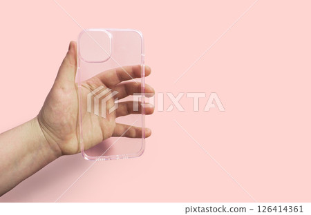 Transparent phone case held in hand against pink background, demonstrating clean design and functionality, ideal for protecting devices while maintaining style and elegance 126414361