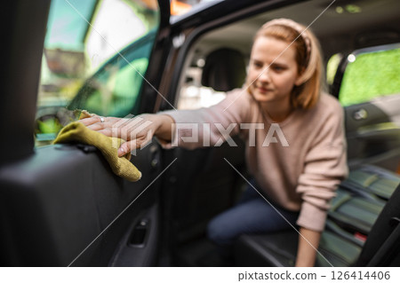 Young woman cleaning car interior with dedication on a sunny day Young woman cleaning car interior with dedication on a sunny day 126414406