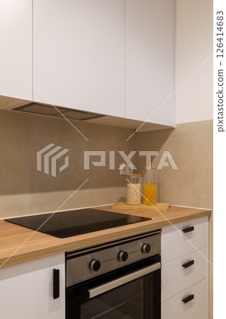 Minimalist kitchen close-up of cooktop and oven with wood countertop, white cabinets and backsplash Minimalist kitchen close-up of cooktop and oven with wood countertop, white cabinets and backsplash 126414683