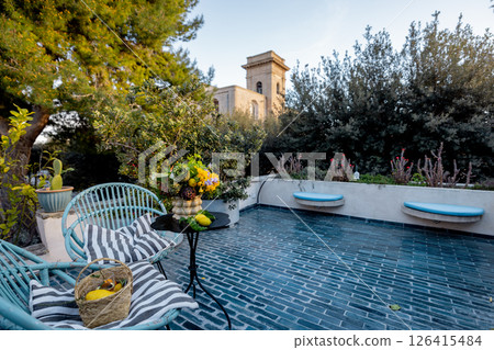 Peaceful terrace with garden chairs and flowers near historic stone tower 126415484