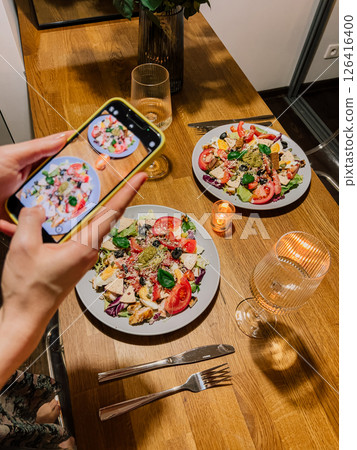 Romantic dinner setup at home with healthy meals, elegant tableware, and warm lighting, capturing the moment of food photography with phone. Cozy dinner scene with two plates of fresh salad at home 126416400