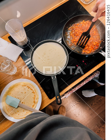 First-person view: person preparing delicious tomato sauce and crepes on electric hob in cozy domestic kitchen, captured from overhead point of view, highlighting culinary process. Tomato, crepes. POV 126416435