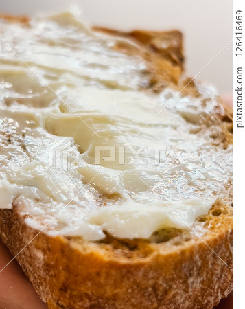 Butter melts on rustic slice, butter adds richness to natural texture, butter spread closeup shows warm homemade feel, bread captures cozy breakfast essence. Spread of creamy butter on crusty slice Butter melts on rustic slice, butter adds richness to natural texture, butter spread closeup shows warm homemade feel, bread captures cozy breakfast essence. Spread of creamy butter on crusty slice 126416469