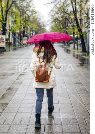 Woman walking with umbrella in empty street during light snowfall. Concept of spring weather, seasonal atmosphere, modern city Woman walking with umbrella in empty street during light snowfall. Concept of spring weather, seasonal atmosphere, modern city 126416666