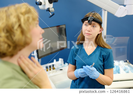 A young woman at an otolaryngologist's appointment talks about pain in the lymph nodes. A professional ENT doctor examines the patient 126416861