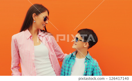 Happy smiling mother with son teenager posing together in casual clothing on orange wall background Happy smiling mother with son teenager posing together in casual clothing on orange wall background 126417140