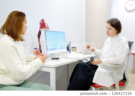 A cardiologist during appointment of patient. Doctor shows EKG on the screen of computer and explains about deviations of heart work. Cardiology consultation and treatment 126417150