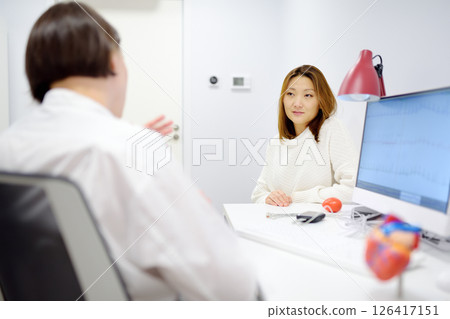 A cardiologist during appointment of patient. Doctor shows EKG on the screen of computer and explains about deviations of heart work. Cardiology consultation and treatment A cardiologist during appointment of patient. Doctor shows EKG on the screen of computer and explains about deviations of heart work. Cardiology consultation and treatment 126417151