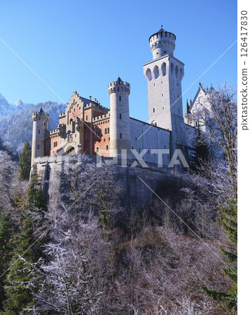 Majestic castle perched on a mountain during winter with snow-covered trees and clear blue sky 126417830