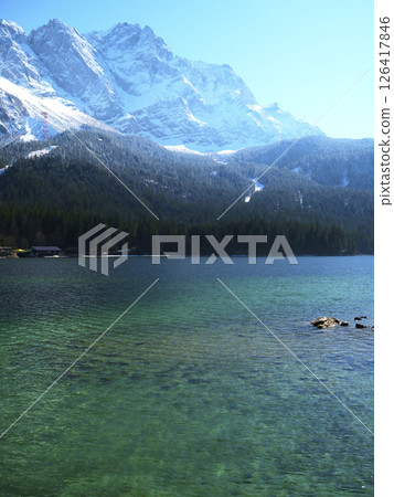 Snow-capped mountains reflect in the clear blue waters of a serene lake surrounded by lush forest Snow-capped mountains reflect in the clear blue waters of a serene lake surrounded by lush forest 126417846