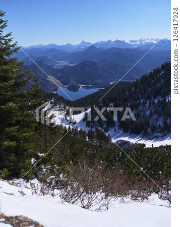Scenic winter view from a mountain overlooking a frozen lake surrounded by snow-capped mountains and evergreen trees Scenic winter view from a mountain overlooking a frozen lake surrounded by snow-capped mountains and evergreen trees 126417928
