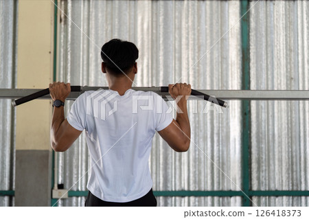Wellness and Fitness. Young man doing pull-ups in gym for strength training. Wellness and Fitness. Young man doing pull-ups in gym for strength training. 126418373