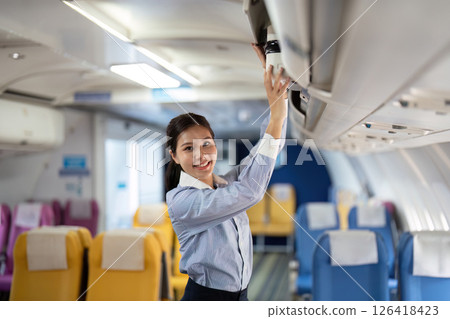 Business travel: Asian woman smiling while placing luggage in overhead bin 126418423