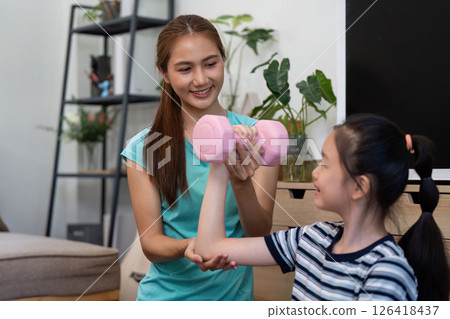 Wellness and Fitness: Mother guiding daughter with weights at home 126418437