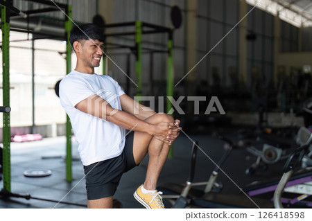 Wellness through Fitness. Young man stretching leg muscles in gym for improved health. Wellness through Fitness. Young man stretching leg muscles in gym for improved health. 126418598