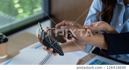 Financial Collaboration. Team members discussing calculations on a calculator during a business meeting. 126418690