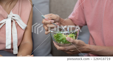 Wellness and Togetherness. Elderly couple feeding each other healthy salad at home. Wellness and Togetherness. Elderly couple feeding each other healthy salad at home. 126418719