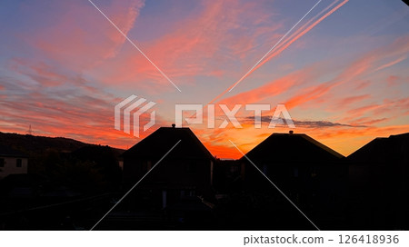 Majestic Sunset Glow Over Suburban Rooftops with Vapor Trails Streaking Across the Evening Sky Majestic Sunset Glow Over Suburban Rooftops with Vapor Trails Streaking Across the Evening Sky 126418936