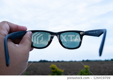 Hand holding stylish sunglasses outdoor field product bright day close-up view Hand holding stylish sunglasses outdoor field product bright day close-up view 126419709