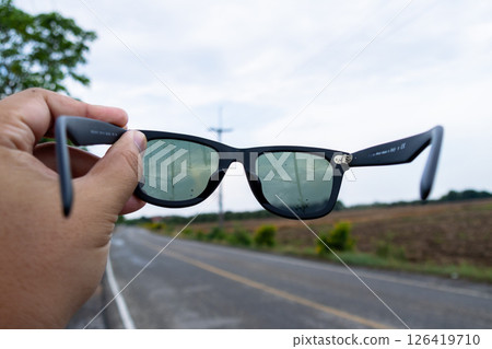 Hand holding sunglasses open road outdoor adventure scenic landscape close-up view Hand holding sunglasses open road outdoor adventure scenic landscape close-up view 126419710