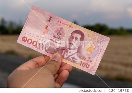 Hand holding thai 100 baht banknote in open field currency outdoor setting 126419788