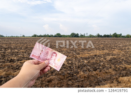 Hand holding currency in agricultural field rural landscape natural environment close-up perspective 126419791
